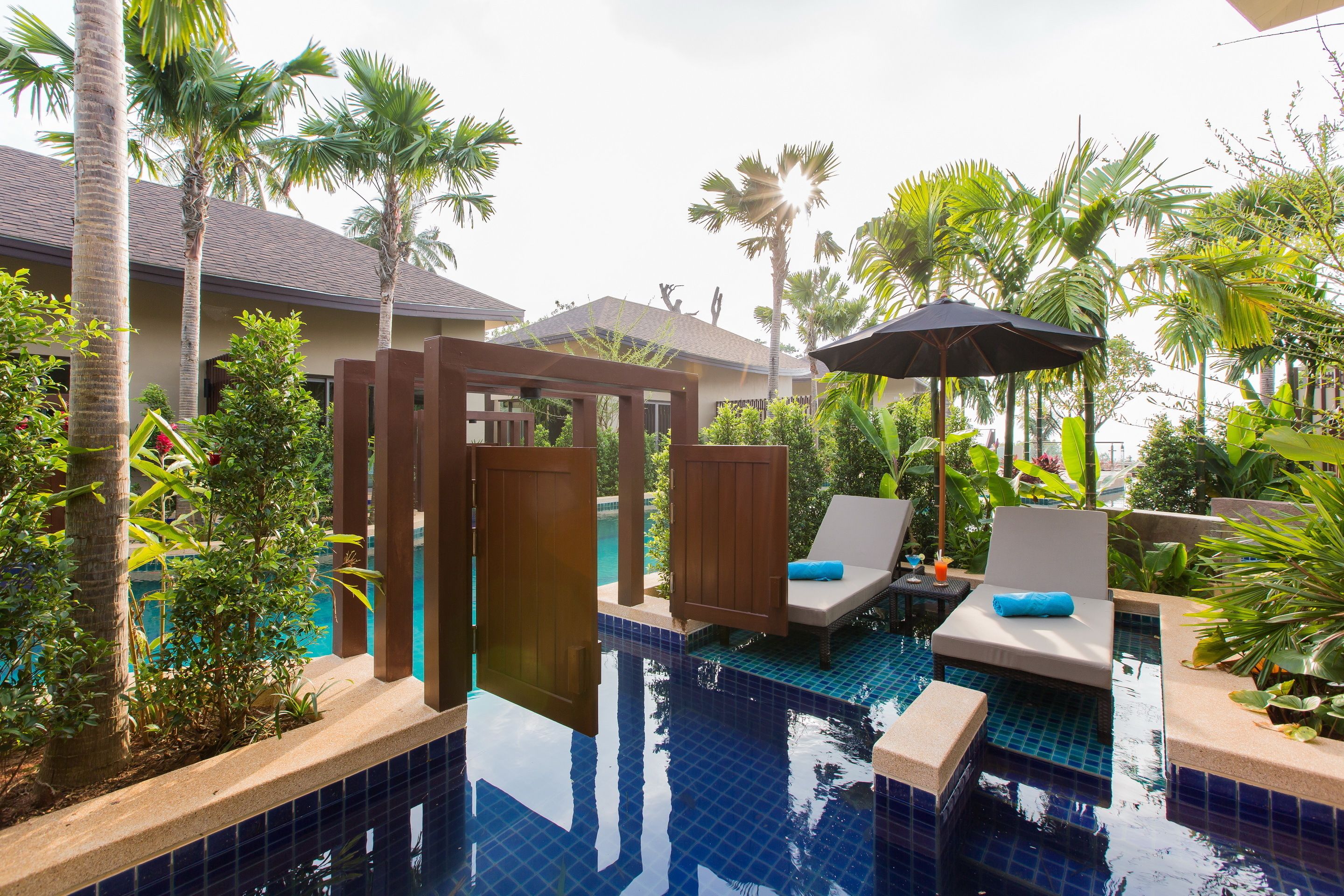 A pool area with lounge chairs, a wooden pergola, and palm trees.