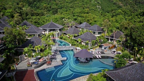 Un complexe hôtelier comprenant plusieurs bâtiments de style bungalow, une piscine centrale au design sinueux et un environnement tropical luxuriant.
