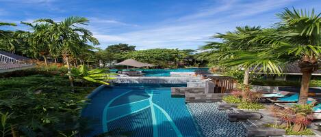 A swimming pool with tiled patterns, surrounded by palm trees and tropical plants.