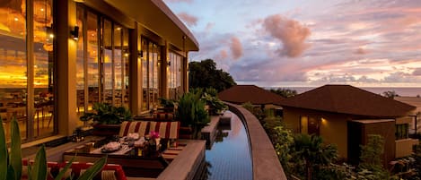 A hotel with a pool, outdoor seating, and a view of the sunset.