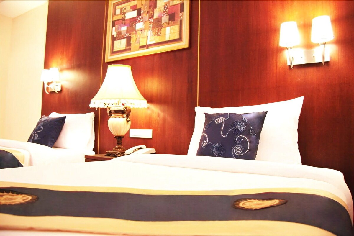 A hotel room with a bed, a bedside lamp, a telephone, and two wall-mounted light fixtures.