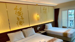 A hotel room with two beds, a wall-mounted light, and a view of the outside.