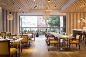A modern dining area with wooden tables and chairs, large windows, and hanging pendant lights. - Hotel Indigo Hong Kong Island by IHG (Hong Kong)