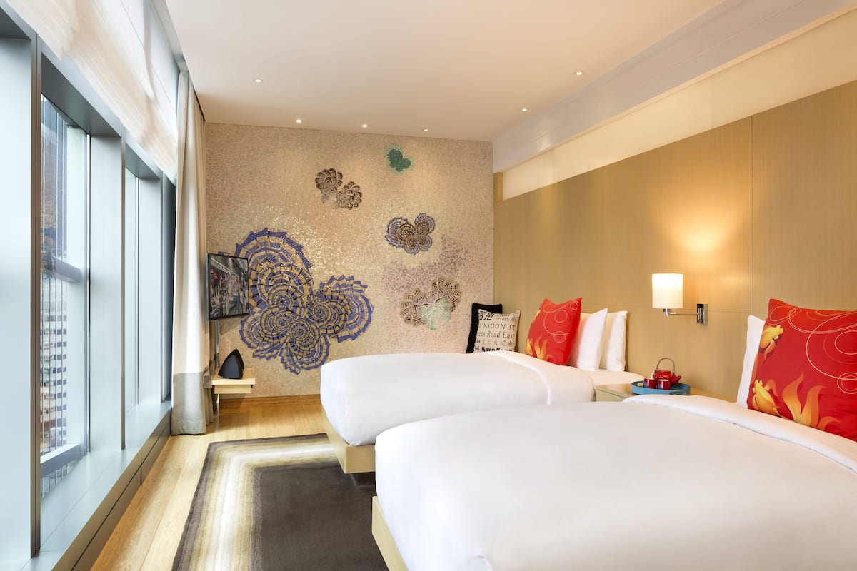 Quarto de hotel com duas camas, uma janela grande e um painel decorativo com motivos florais.