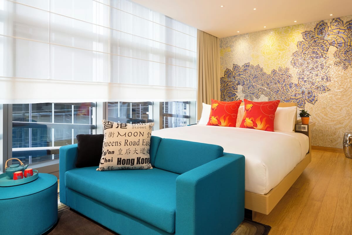 Quarto de hotel moderno com uma cama grande, um sofá azul e vista para a cidade.