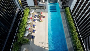 A rooftop pool with lounge chairs and umbrellas, surrounded by high-rise buildings. - Hotel Indigo Hong Kong Island by IHG (Hong Kong)