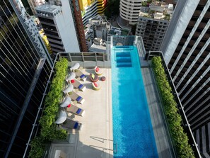 A rooftop pool with lounge chairs and umbrellas, surrounded by high-rise buildings. - Hotel Indigo Hong Kong Island by IHG (Hong Kong)