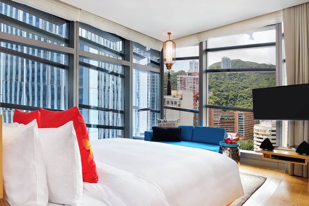 Quarto de hotel moderno com uma cama grande, um sofá azul e uma televisão.