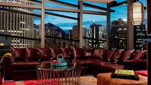 A modern living room with a leather sofa, a round coffee table, and a view of a cityscape at dusk. - Hotel Indigo Hong Kong Island by IHG (Hong Kong)