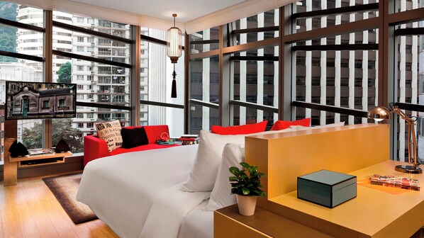 A modern hotel room with a large bed, red and white furnishings, a desk with a lamp, and a view of a cityscape through floor-to-ceiling windows. - Hotel Indigo Hong Kong Island by IHG (Hong Kong)
