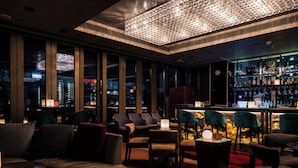 A modern bar area with leather seating, a well-lit chandelier, and a city view through large windows. - Hotel Indigo Hong Kong Island by IHG (Hong Kong)