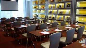 A conference room with tables and chairs, a projector screen, and a bookshelf with books and decorative items.