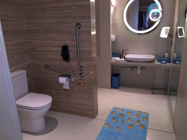A modern bathroom with a toilet, a shower with a glass door, a sink with a mirror, and a blue mat with animal prints.