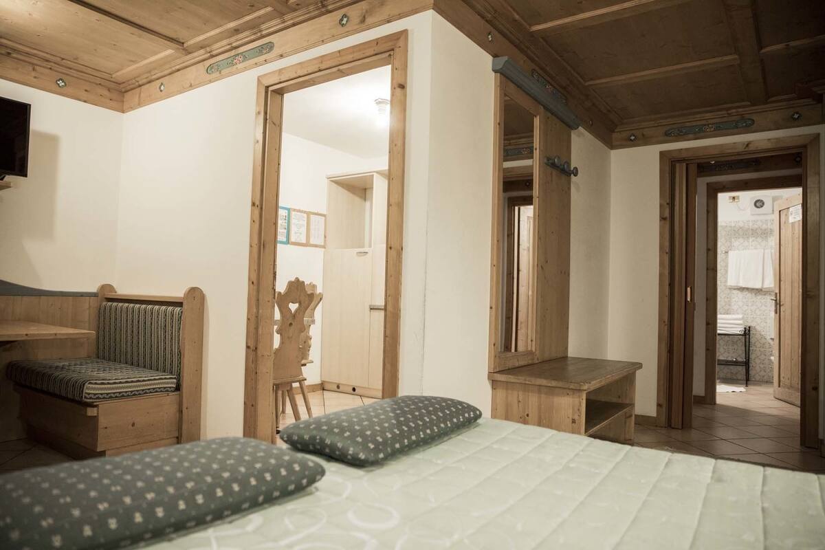 A room with a bed, a wooden bench, a chair, and a mirror.