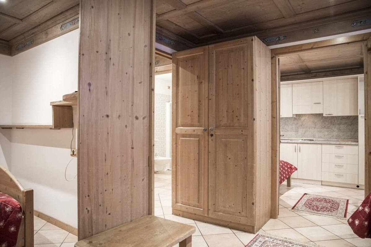 A room with a wooden bench, a wardrobe, and a kitchen area with cabinets and a countertop.