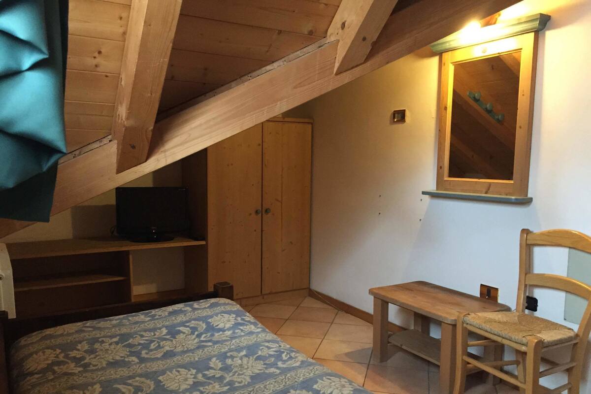 A bedroom with a bed, a wooden chair, a small table, a television, and a wardrobe.