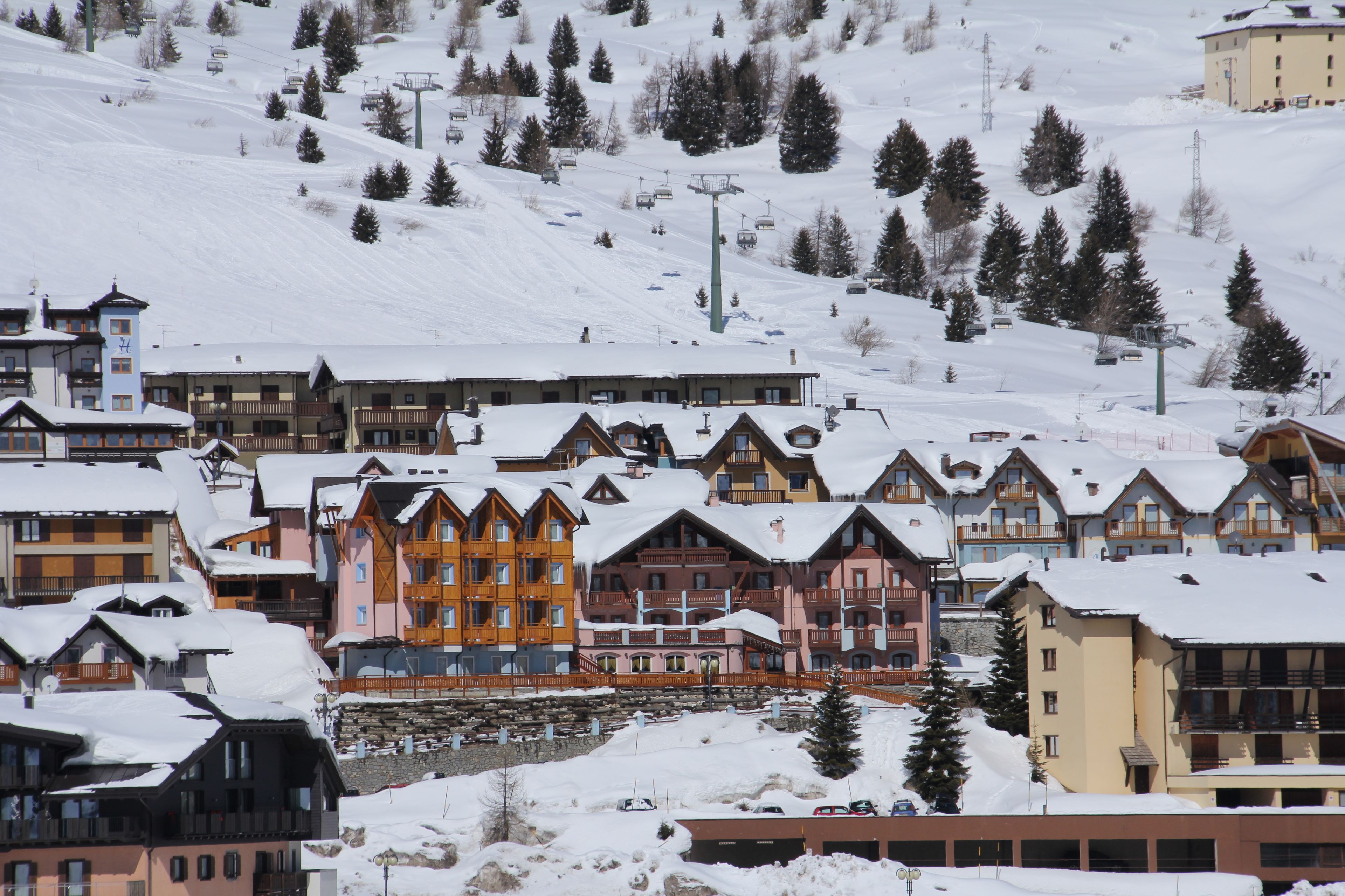 Un centro de esquí cubierto de nieve con edificios de varios pisos, telesillas y montañas al fondo.