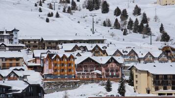 Un centro de esquí cubierto de nieve con edificios de varios pisos, telesillas y montañas al fondo.