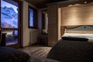 A bedroom with a large window, wooden headboard, and a bed with patterned bedding. - Dahù Hotel Residence (Vermiglio)