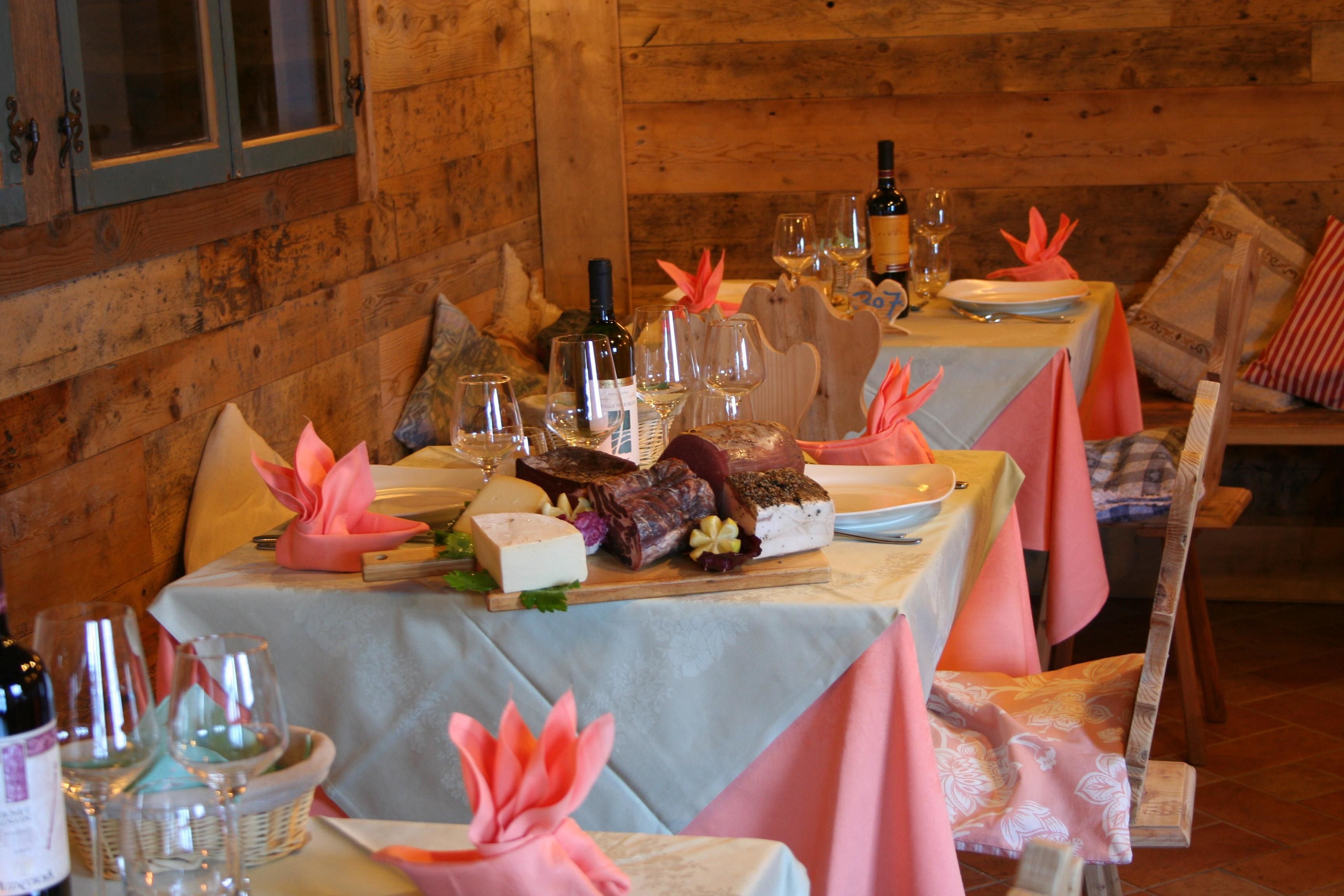 A long dining table with a white tablecloth, set with wine glasses, plates, and a variety of cheeses and meats.