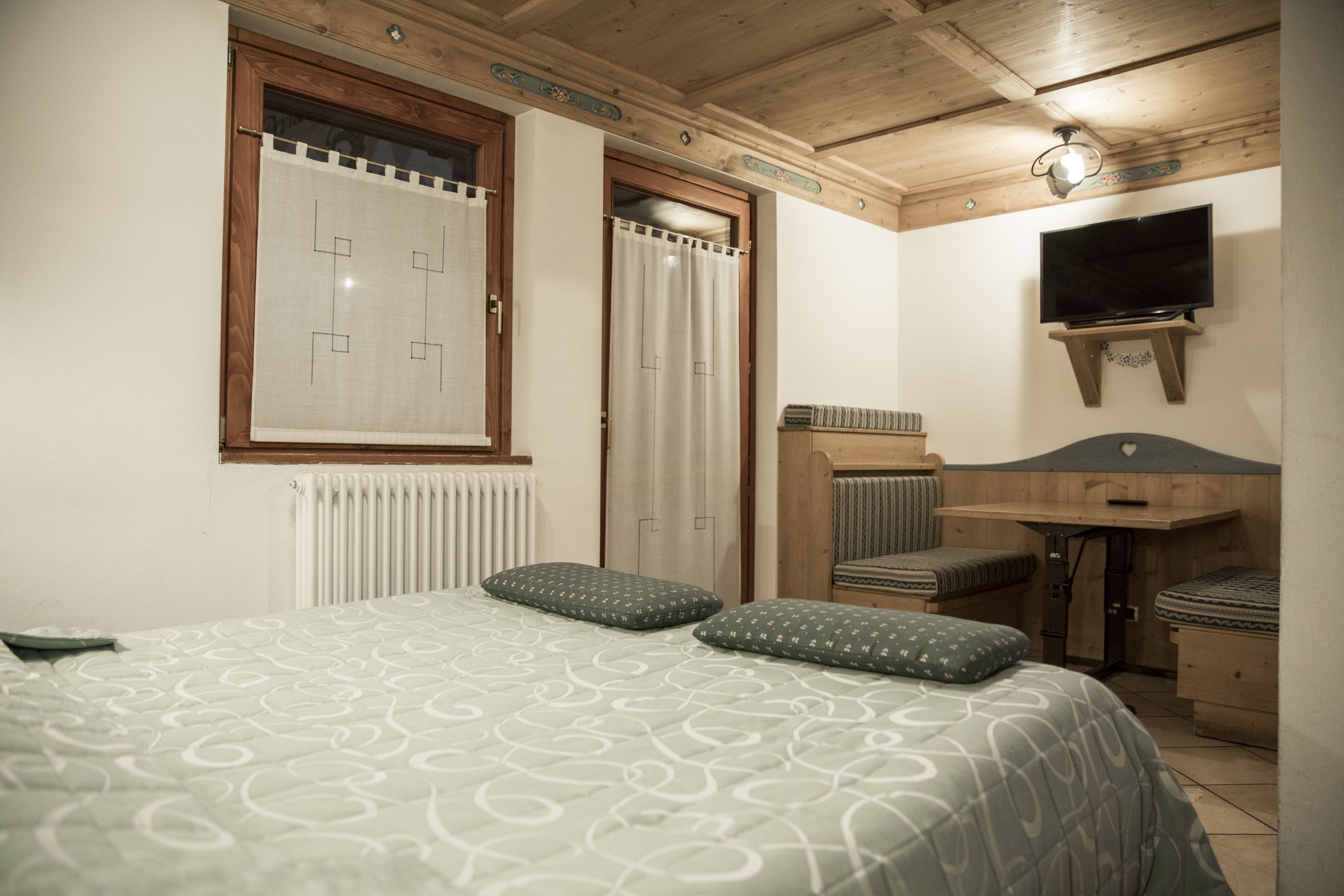 A bedroom with a bed, pillows, a TV, a desk, and a radiator.