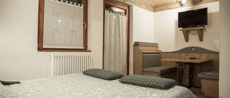 A bedroom with a bed, pillows, a TV, a desk, and a radiator.