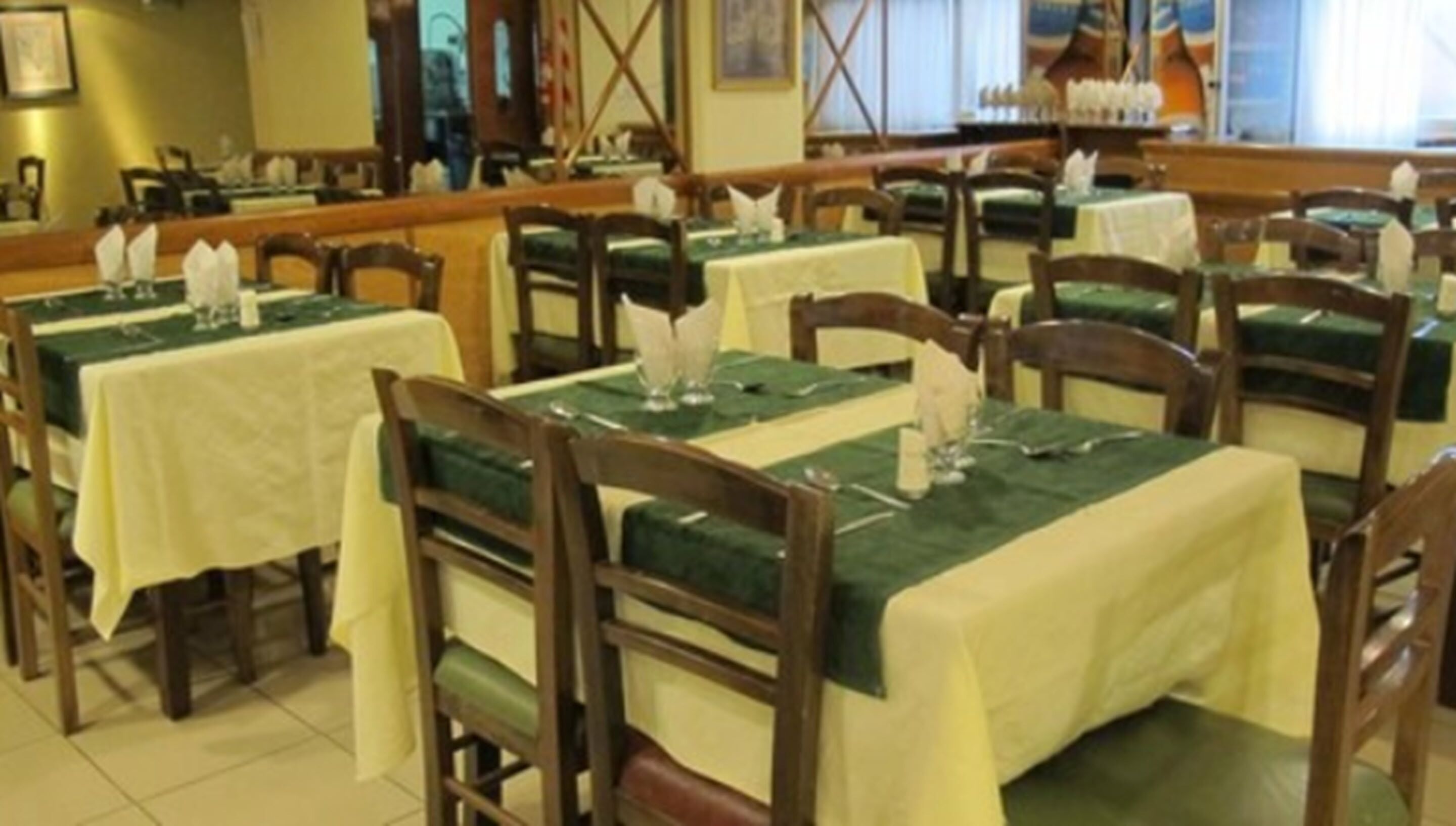 A restaurant with multiple tables covered with green tablecloths and wooden chairs.