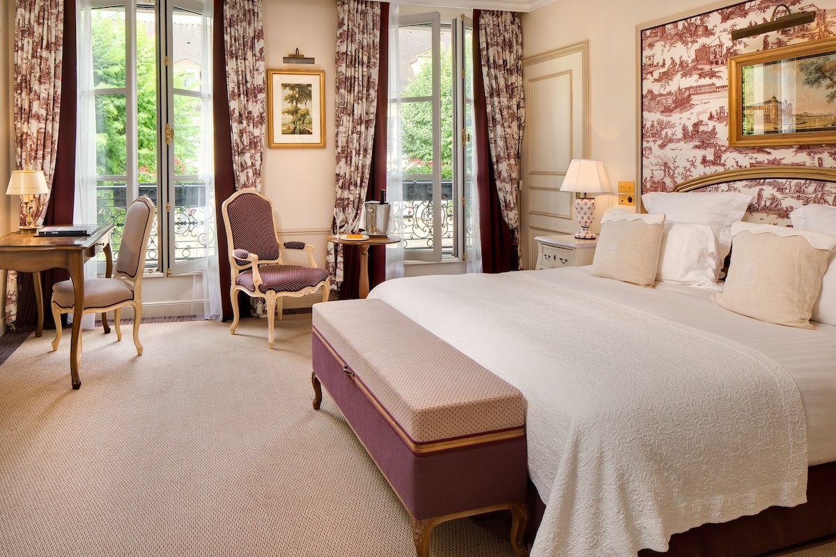 Ein Hotelzimmer mit einem großen Bett, einem Schreibtisch, einem Stuhl und Blick auf Grünflächen durch das Fenster.