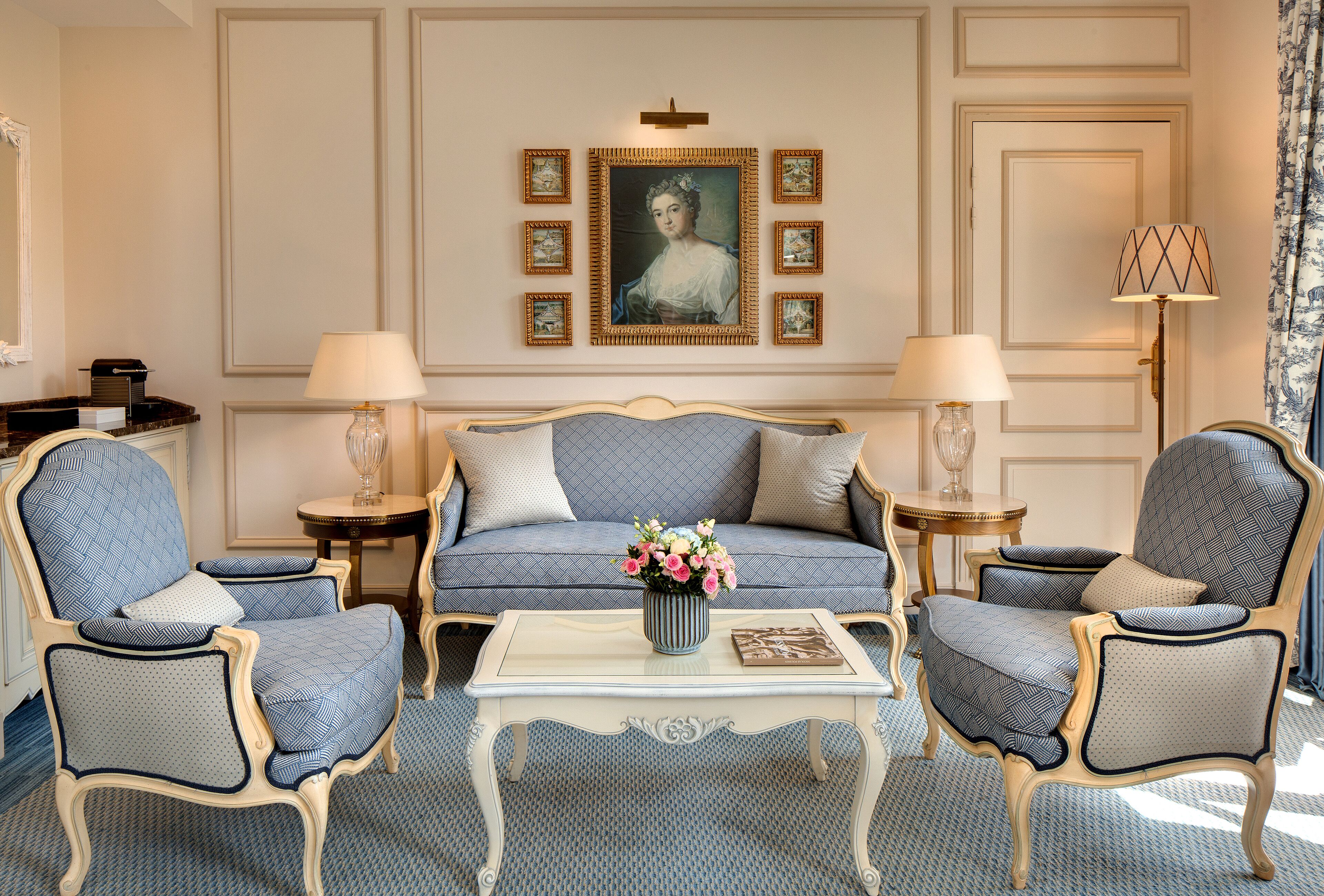 Une pièce comprenant un canapé, deux fauteuils, une table basse, un vase avec des fleurs, des tableaux encadrés accrochés au mur et une lampe.