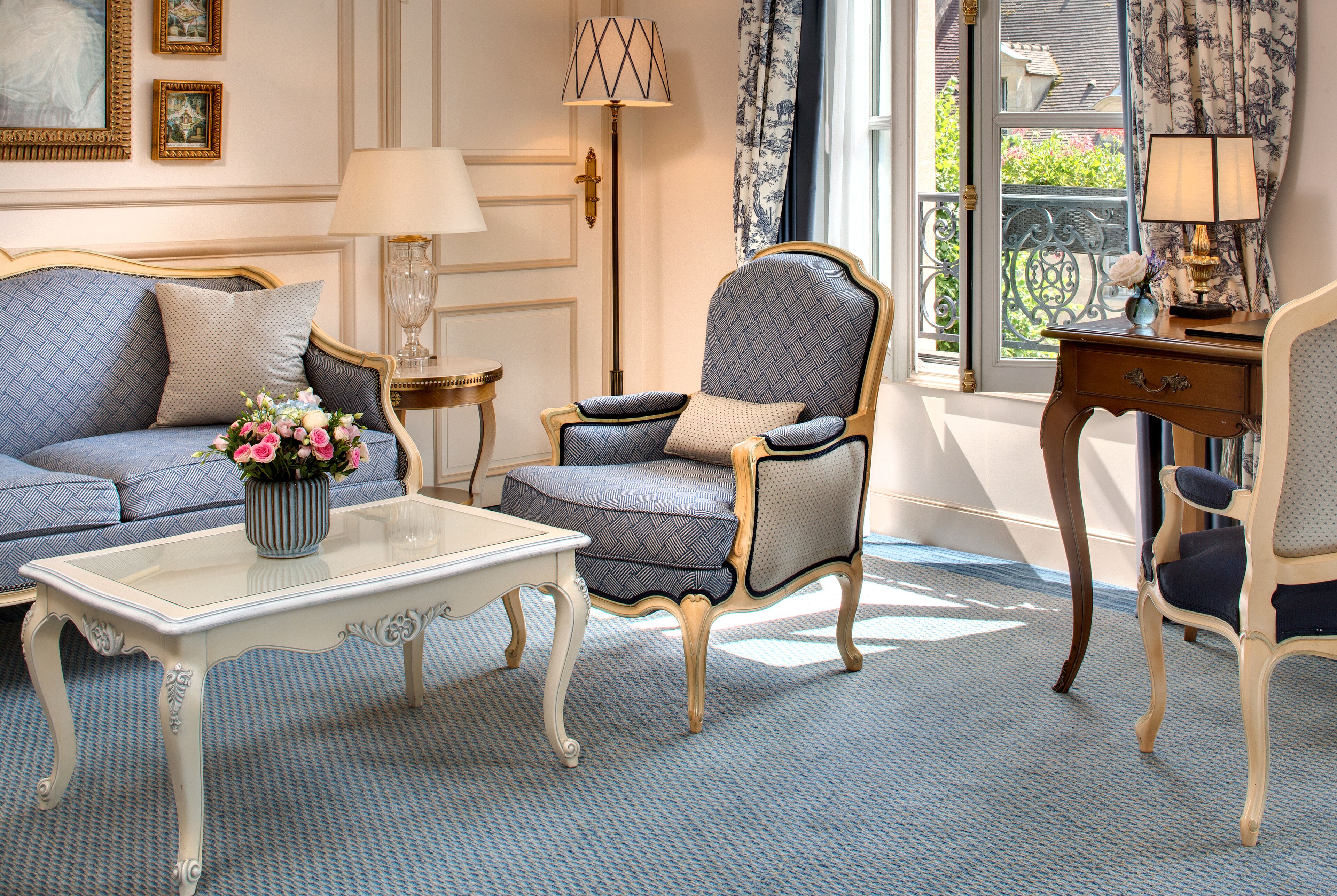 A room with a sofa, armchair, and a small table with a vase of flowers.