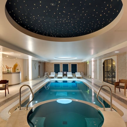 A modern indoor pool with a starry ceiling, lounge chairs, and a central seating area.