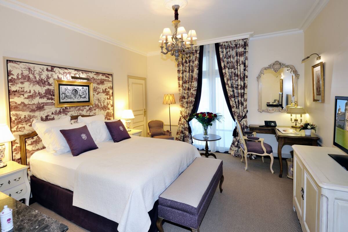 Ein Hotelzimmer mit einem großen Bett, einem Schreibtisch, einem Stuhl, einer Kommode und einer Chandelier.