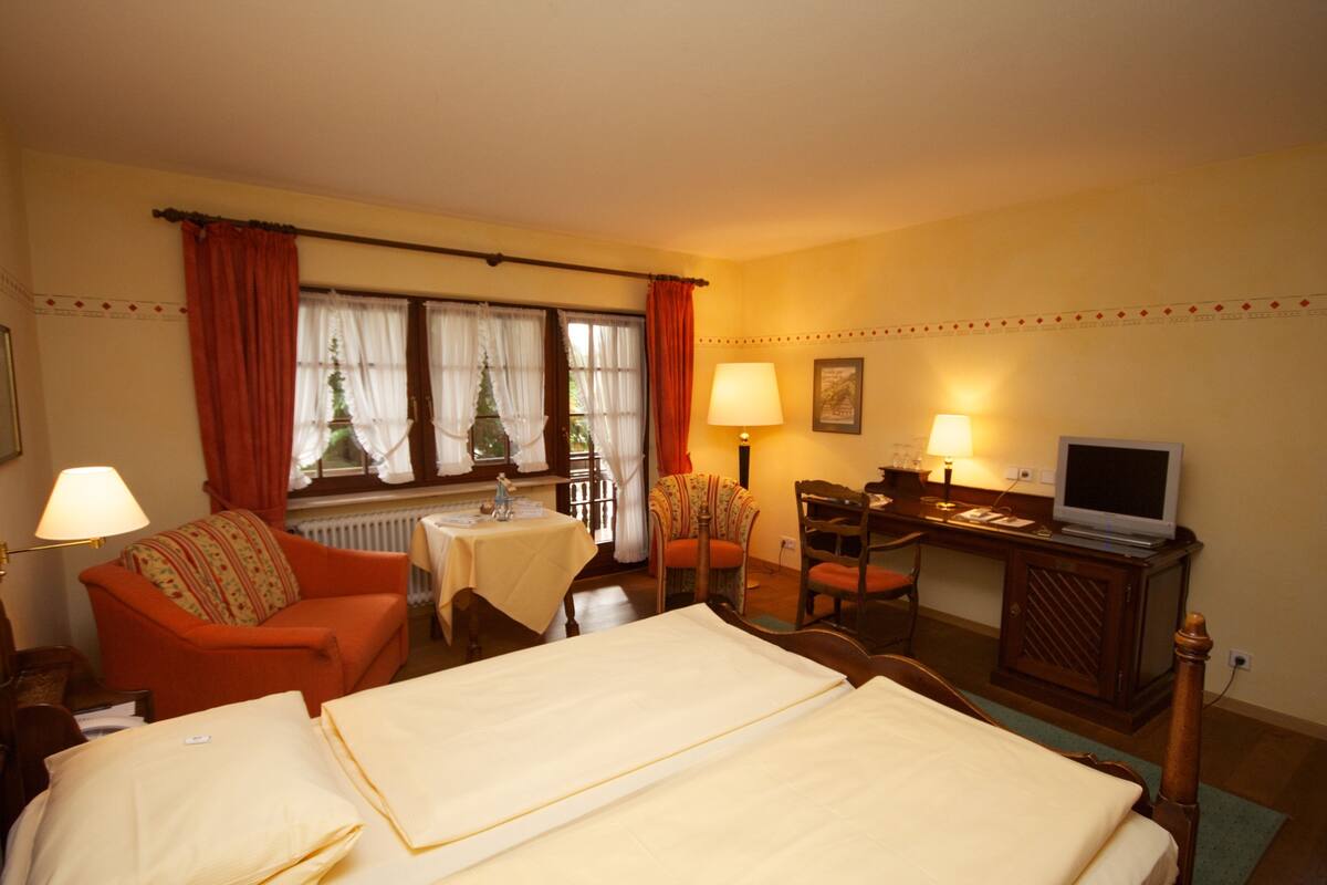 A hotel room with a bed, a desk with a computer, a chair, a small table with a lamp, and a television.