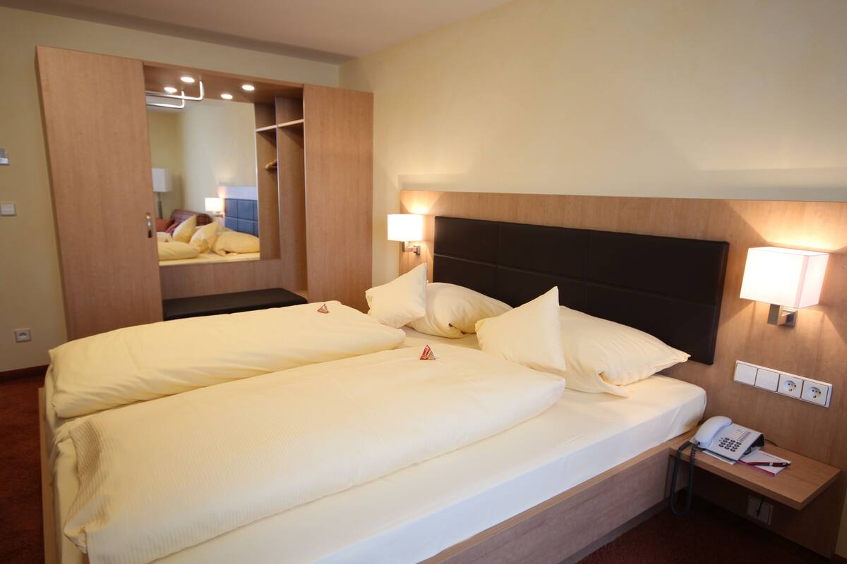 A double bed with a wooden headboard, two bedside lamps, a bedside phone, and a mirror above the bed.
