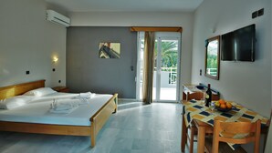 A hotel room with a bed, a dining table with chairs, a TV, and a balcony with a view. - Hotel Athena (Apokoronas)