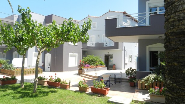 A courtyard with a lawn, potted plants, and a seating area with a table and chairs. - Hotel Athena (Apokoronas)