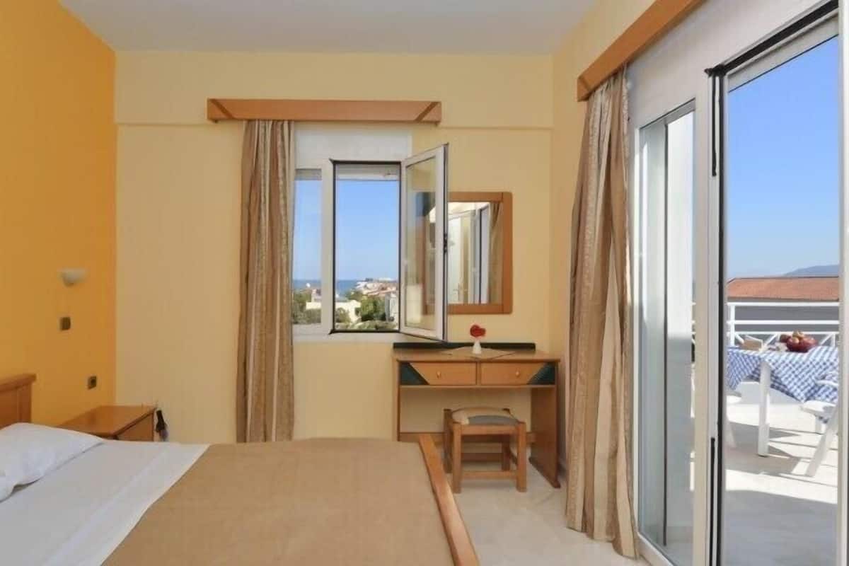 A hotel room with a bed, a desk, a chair, a large mirror, and a sliding glass door leading to an outdoor area with a table and chairs.