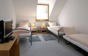 Un dormitorio ático pequeño y triangular con dos camas individuales, un escritorio con computadora y una ventana que proporciona luz natural.