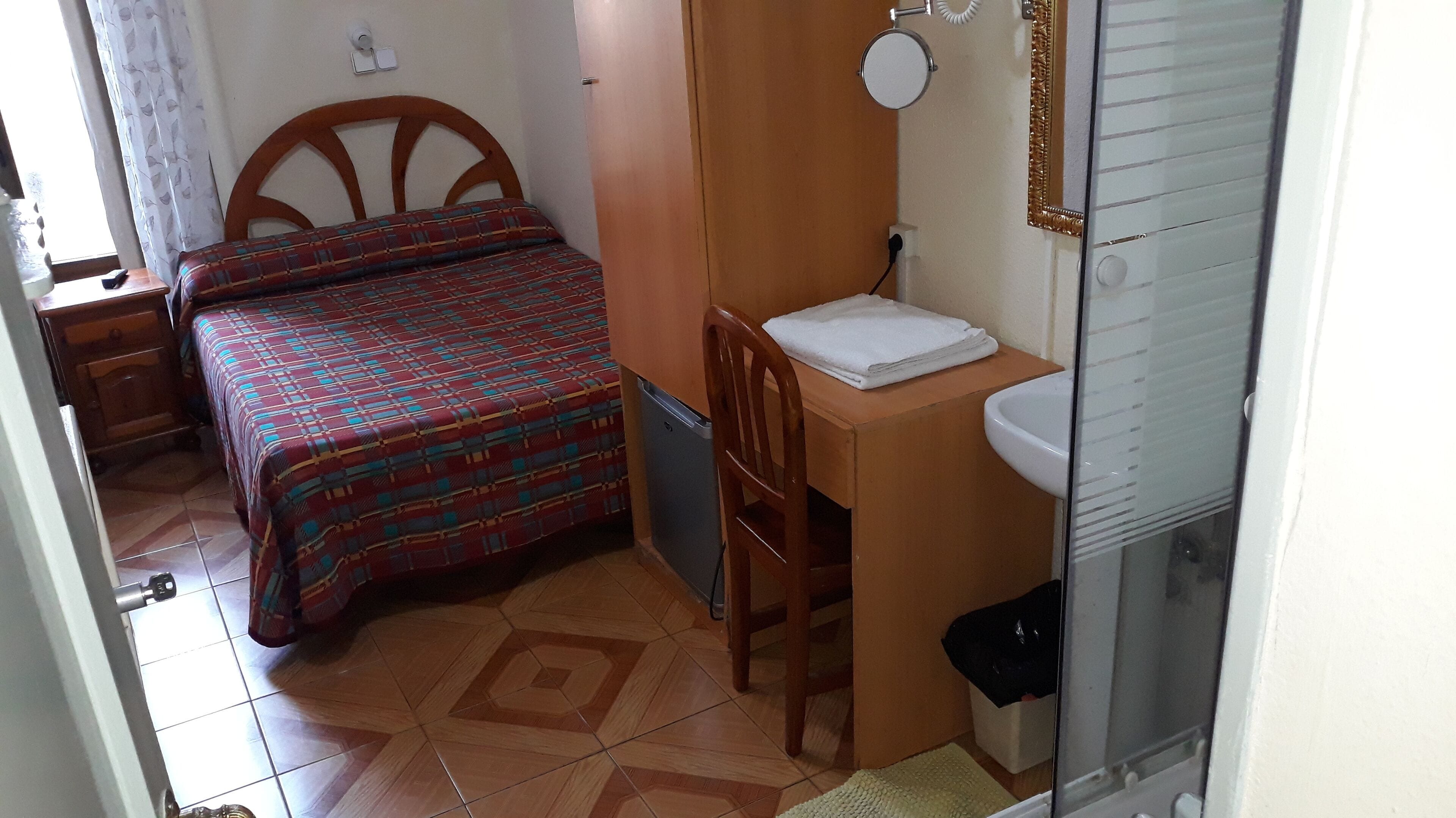 A small, compact room with a bed, a desk with a sink, and a chair.