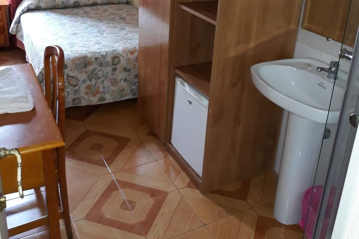 Habitació compacta amb un llit, un armari de fusta, un petit rentatòri i un sòl de rajola.