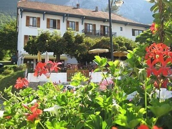 Un edificio blanco con techo de tejas, rodeado de exuberante follaje y flores rojas.