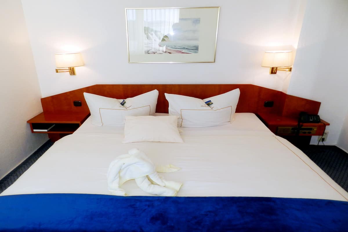 Una habitación de hotel con una cama grande, dos mesitas de noche, una pintura en la pared y dos lámparas de pared.