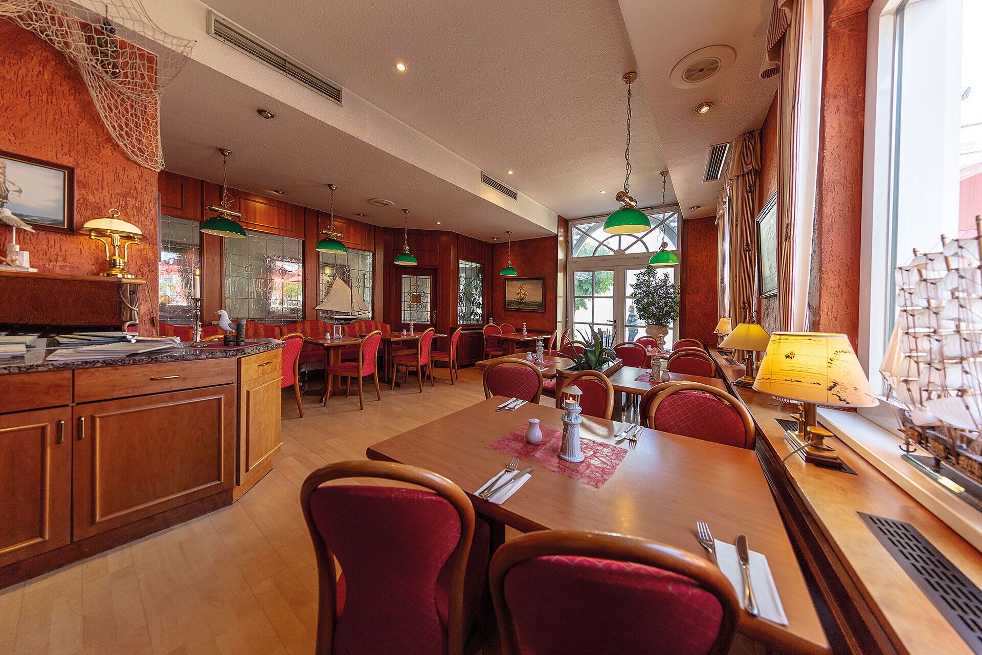 A restaurant with wooden furniture, green hanging lamps, and large windows.