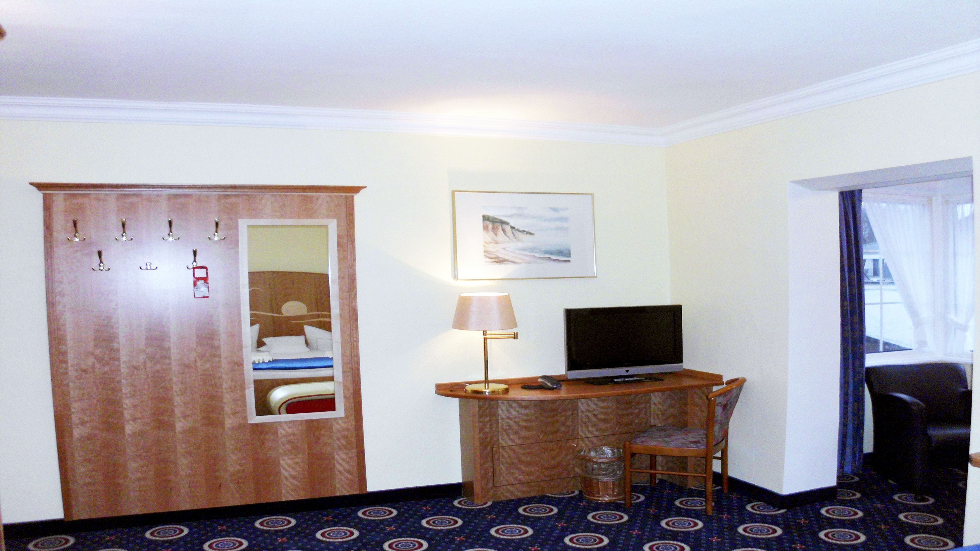 Ein Hotelzimmer mit einem Bett, einem Schreibtisch mit Computer, einem Sessel, einem Fernseher, einer Lampe und einem Kleiderschrank.