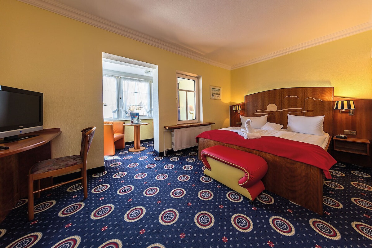 Una habitación de hotel con cama, televisión, escritorio y dos ventanas.