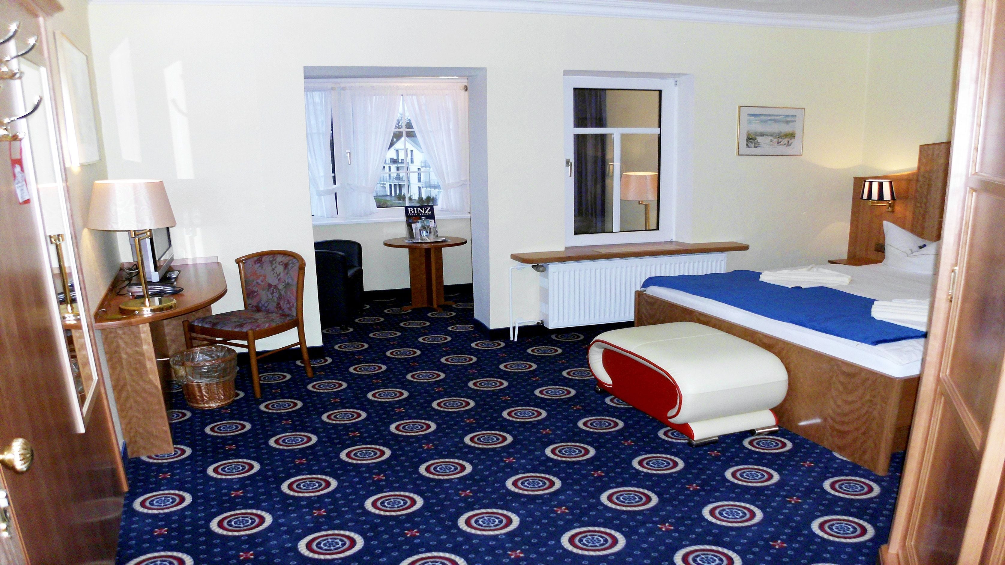 Habitación de hotel con cama, una silla, una mesita, una lámpara y ventana con cortinas.