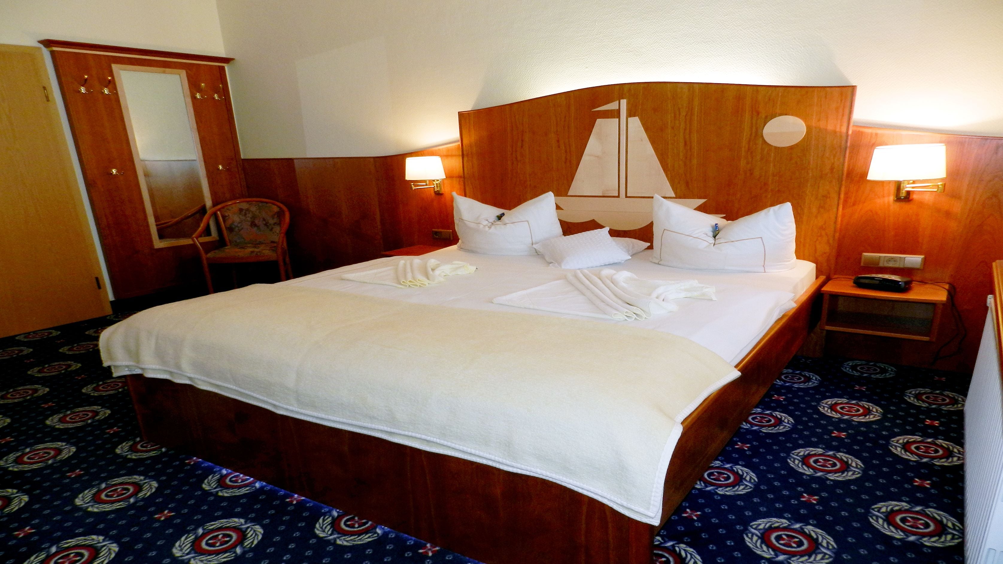 Una habitación de hotel con una cama grande, dos mesitas de noche, un cabecero de madera, un espejo y una alfombra estampada.