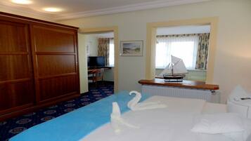 A hotel room with a bed, a wooden wardrobe, a desk with a television, and a sailboat model on the dresser.