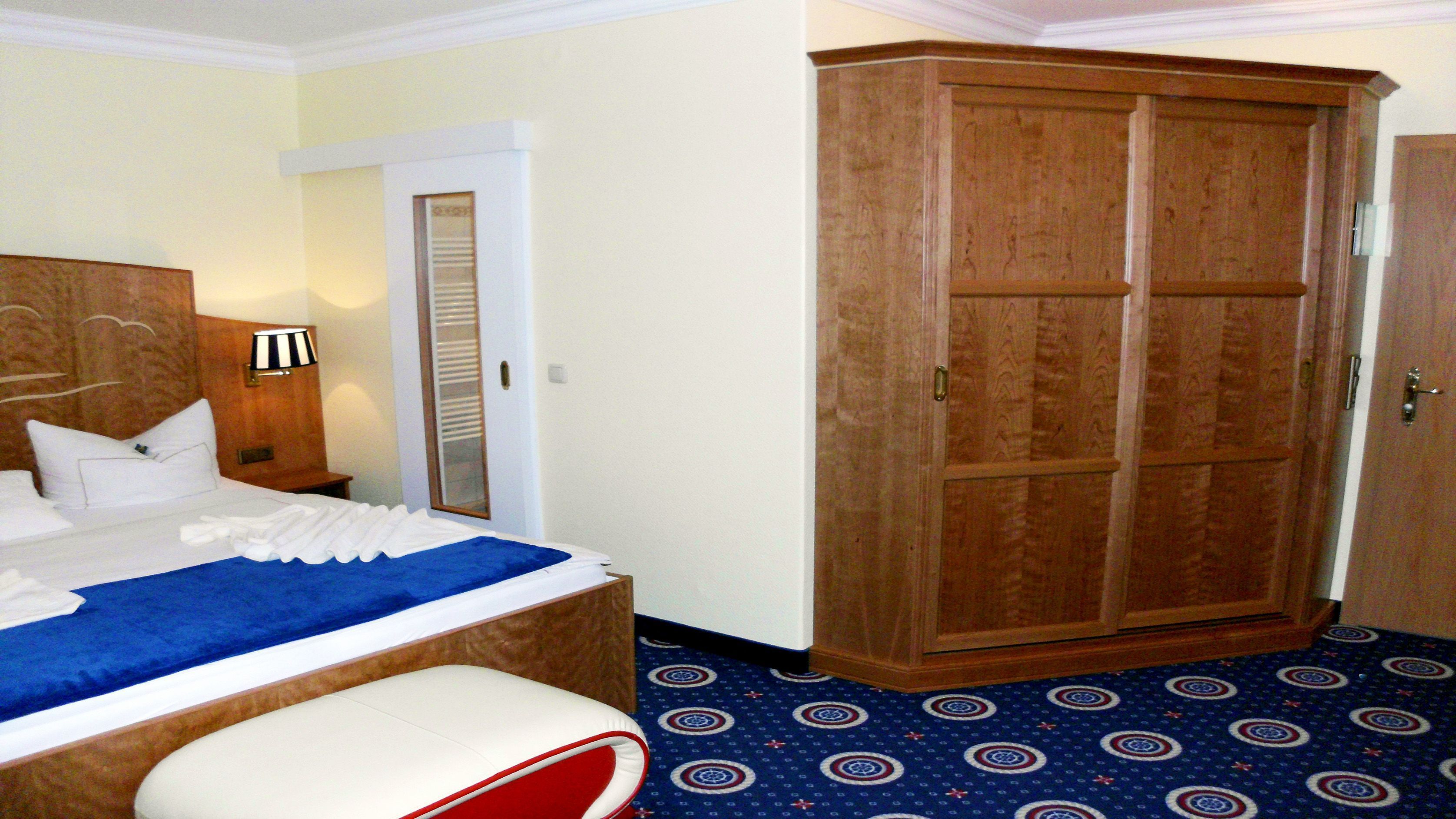 A hotel room with a bed, a wardrobe, and a patterned carpet.