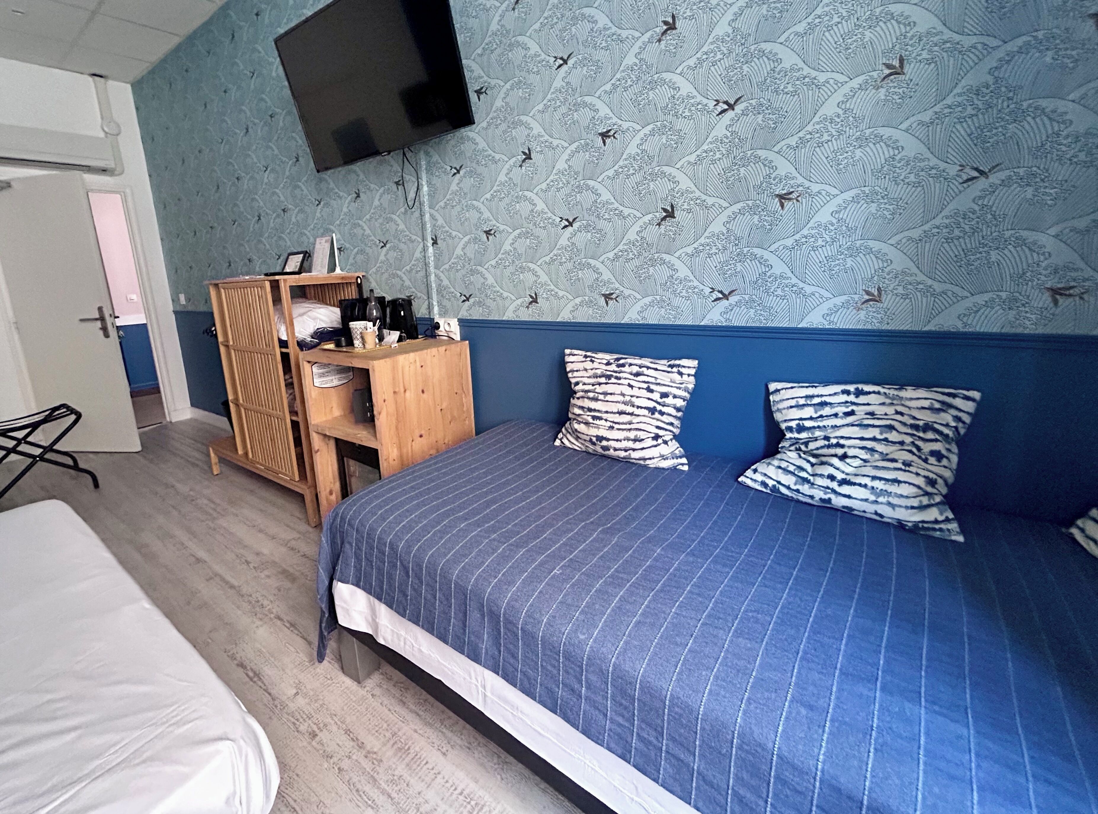Una habitación con cama, un armario de madera, un televisor en la pared y un papel tapiz estampado.